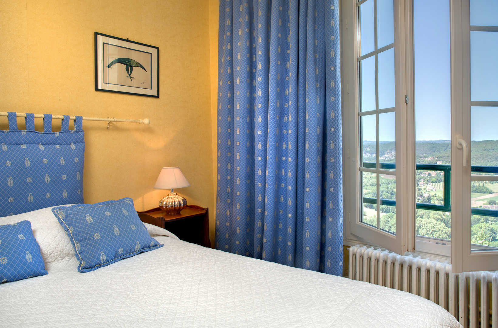 Vue intérieure sur une chambre confortable aux murs jaunes et aux rideaux bleus dans l'hôtel en Périgord, Domme - Hôtel L'Esplanade